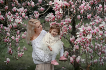Portrait of happy joyful child in white clothes over tree flowers blossom background. Family playing together outside. Mom cheerfully hold little daughter Newborn spring concept