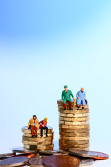 Conceptual diorama image of a miniture figure retired couple and young couple sat on a stack of...
