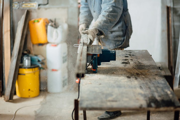 man in work clothes by profession carpenter handles wooden board on circular saw on a wooden workshop table, joiner works on machine in factory