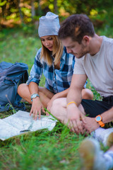 Young couple resting and checking the map inside the forest. Hiking concept in the mountain in summer