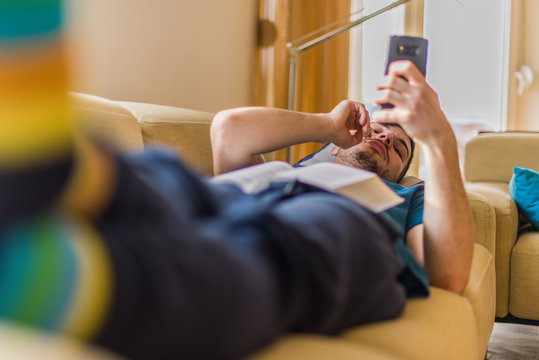 Young guy lying at the couch and hold mobile