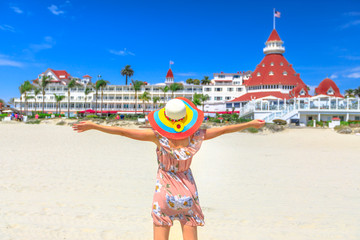 Carefree woman in hat on Coronado Central Beach, looking historic Victorian hotel on Coronado...
