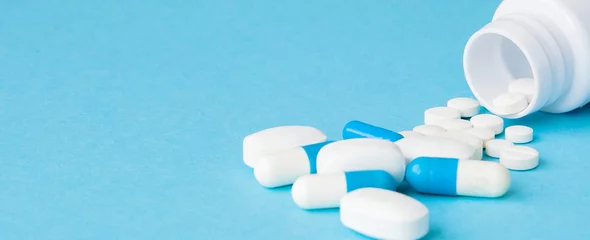 Foto auf Acrylglas Apotheke Nahaufnahme von Pillen, die aus der Pilleflasche auf blauem Hintergrund verschüttet werden. Medizin-, Krankenversicherungs- oder Apothekenkonzept