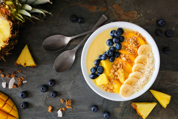 Healthy pineapple, mango smoothie bowl with coconut, bananas, blueberries and granola. Top view...