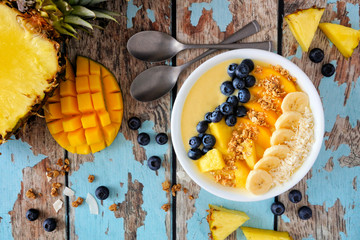 Healthy pineapple, mango smoothie bowl with coconut, bananas, blueberries and granola. Top view...