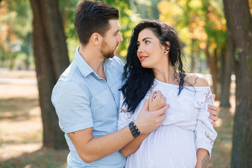 Obraz premium Pregnant girl walks in the park with her husband, hugging and kissing, enjoying the beautiful weather