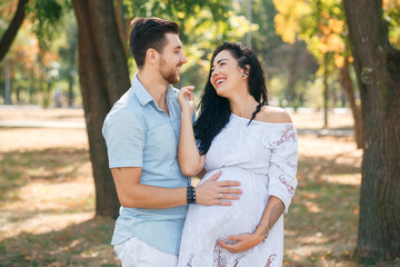 Obraz premium Pregnant girl walks in the park with her husband, hugging and kissing, enjoying the beautiful weather