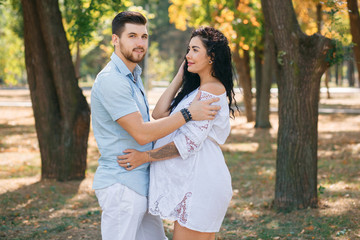 Fototapeta premium Pregnant girl walks in the park with her husband, hugging and kissing, enjoying the beautiful weather