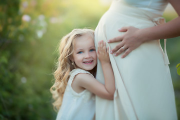 Happy family: a young beautiful pregnant woman with her little cute daughter walking in the wheat orange field on a sunny summer day. Parents and kids relationship. Nature in the country.