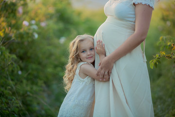 Fototapeta na wymiar Happy pregnant woman with little daughter in a green tea rose garden