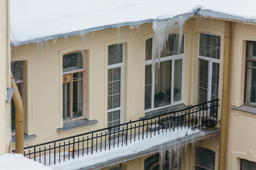 Photo of big icicles hanging from building, many people get injured by the drop of icicles/ poor attic insulation, danger for humans, long icicles hang from the roof of a house, winter concept.