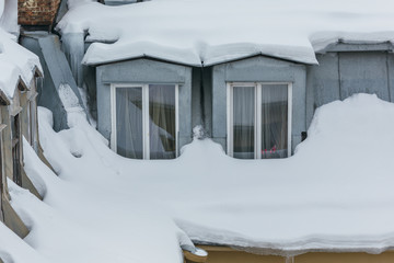 Cropped photo of snow-covered windows in the attic apartment, roof leak, roof cover damage, high precipitation, danger of falling snow on a person, roof is covered with snow, winter concept