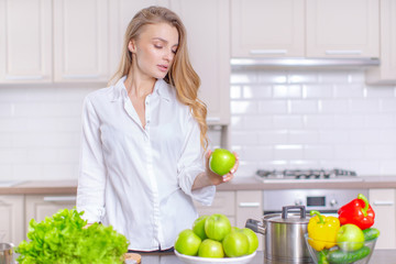 Beautiful young girl in the kitchen holding a green apple