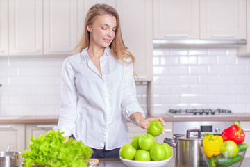 Beautiful young girl in the kitchen holding a green apple