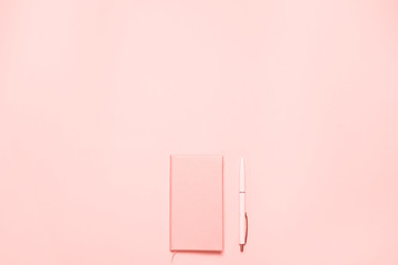 Trendy Coral colored desk with coral colored diary and pen. Minimalistic flat lay composition with...