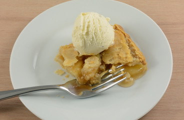 Slice of apple pie with scoop of French vanilla ice cream on white dessert plate with fork
