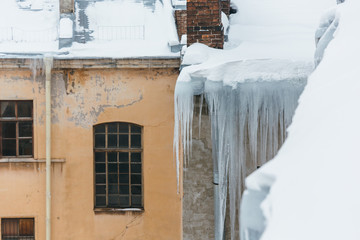 Huge human sized icicles hang from a residential building, during the thaw the ice can break off and cripple a person/ danger for humans, long icicles hang from the roof of a house, winter concept
