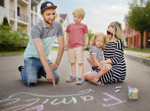Happy amicable family with two children walking in summer. The word "family" painted with colored chalk on asphalt.