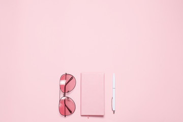 Pink diary, glasses and pen on pink desk. Flat lay, top view. Copy space.