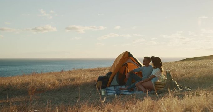Attractive hipster couple looking out at sea and pointing, summer surf camping adventure