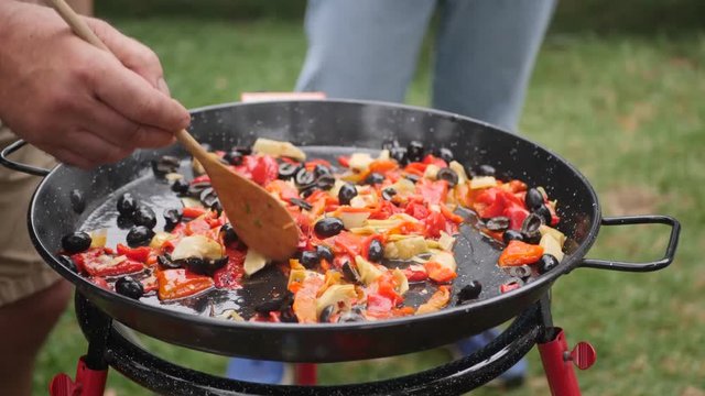 Shot of a man preparing a traditional paella in a garden.