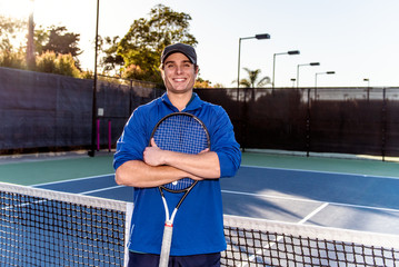 Young and good looking tennis teaching professional showing smile and happy expression on the tennis court.