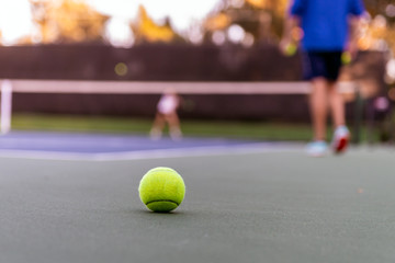 Lone yellow tennis ball lying out of bounds during a private racket club tennis lesson.