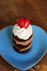Red candy heart on whipped cream over a round chocolate mini cake