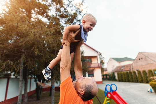 Grandfather lifting up his grandson and playing with him. Countryside exterior.
