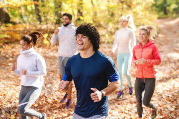 Five cheerful runners in sportswear running in forest at autumn Fitness in nature concept. Side view.