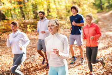 Five cheerful runners in sportswear running in forest at autumn Fitness in nature concept. Side view.