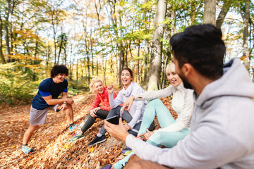 Small group of sporty people sitting in forrest in autumn and resting from running and exercising. Fitness in nature concept.