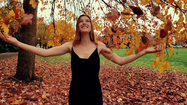 Slow motion shot of young woman throwing brown autumnal leaves in the air above her head