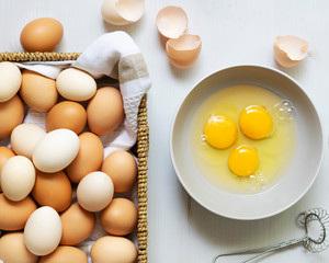 Brown and white eggs in a basket and raw eggs in a bowl.