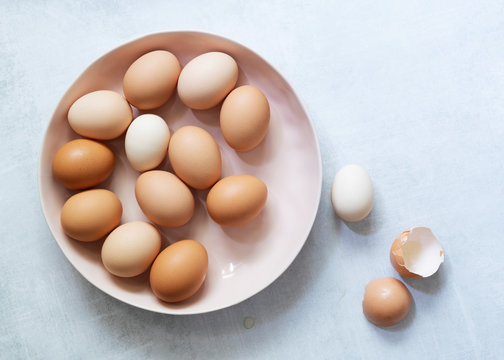 Brown and white eggs in a bowl with egg shells at the side.