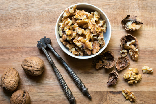 Cracked walnut pieces in a bowl beside whole walnuts and a vintage nut cracker.