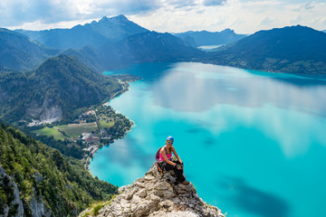 Exhausted but happy girl taking a break on a rock cliff above the turquise waters of Attersee lake,...