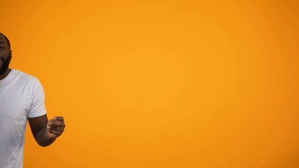 Afro-American man dancing against yellow background, feeling rhythm of music