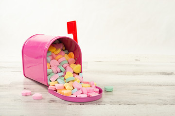 Pink mailbox full of candy conversation hearts on a wood table with a shallow depth of field and...