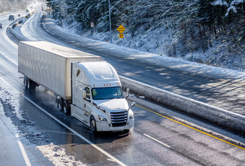 Big rig white bonnet semi truck with dry van semi trailer moving on the winding winter road with...