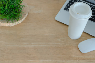 Wooden desk in office with laptop computer, white mouse, coffee tumbler and Tillandsia airplant which is modern plant that no need much water, decorate on the desk. Top view with space for text.