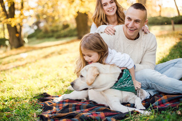 Fototapeta premium Happy beautiful family with dog labrador is having fun are sitting on green grass in park.