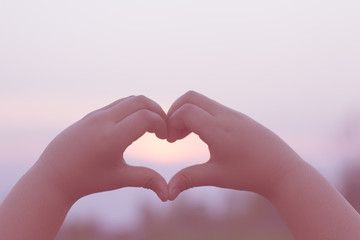 Fototapeta premium The silhouette of a kids hand in a beautiful sunrise captures the sun in the heart.