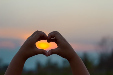 The silhouette of a kids hand in a beautiful sunrise captures the sun in the heart.