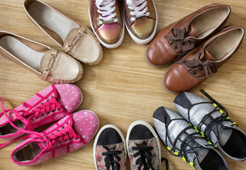 Various women's shoes and sneakers stand in the form of a circle with a free space in the middle, on a wooden background.