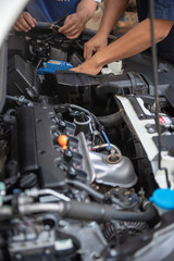 Car service by an auto mechanic in garage, fixing a car battery with wrench, also checking some parts of the engine showing by selective focus.