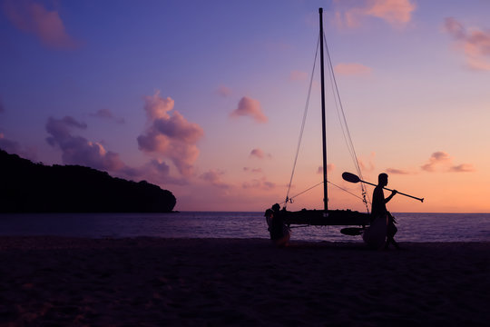 Silhouette Asian Man With Paddle And Sailing Catamaran On The Beach