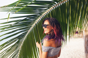 Attractive young slim woman with multi-colored hair in sunglasses on the background of palm trees, beauty fashion and travel concept