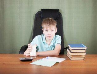 Cute schoolboy sitting at table with apple and doing homework