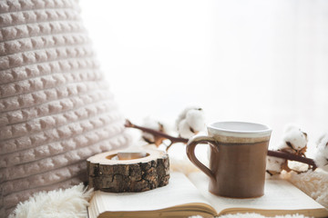 Details of still life in the home interior. Beautiful tea Cup, cut wood, book and pillows, cotton flower on a windowsill. Vintage, rustic. Cosy autumn-winter concept. Copy space